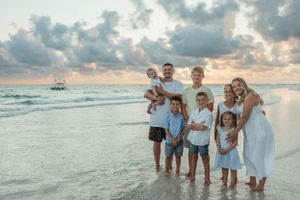 Extended family group standing together in the ocean surf during sunset at the beach.