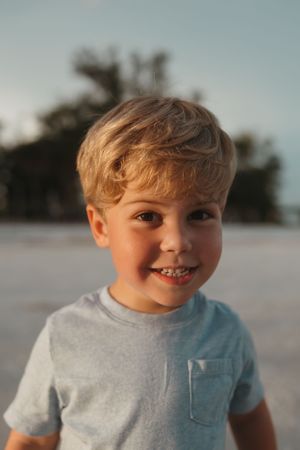 Close-up portrait of a young boy smiling at sunset on the beach.