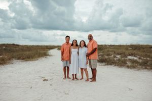 A family of four poses together on white sand beach dunes under dramatic cloudy skies.