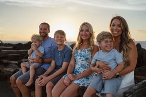 A family sits together on rocky coastline during sunset.