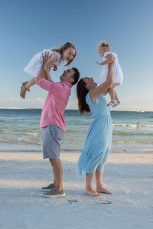 Parents lift and play with children on a sunny beach.