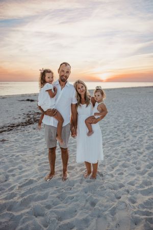 Group in white outfits poses on sandy beach during golden sunset.