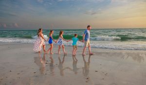 Five people hold hands while walking along the beach at sunset.