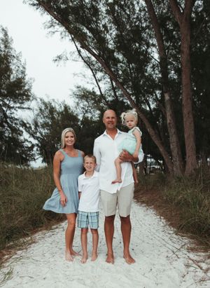 Family portrait on sandy beach path with tall trees in background.