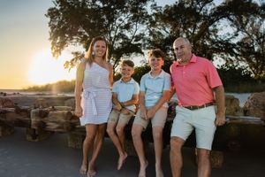 Family of four sitting together on rocks at sunset.