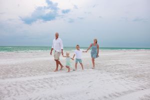 Family holding hands while walking on white sandy beach with turquoise water.