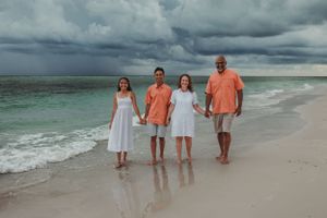 A group of four people dressed in white and coral stand together on a beach at sunset.