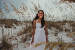 A person in a white dress poses among beach grass and sand dunes.