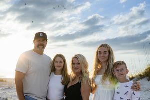 Family portrait at sunset on a sandy beach with grass and dramatic clouds in the background.