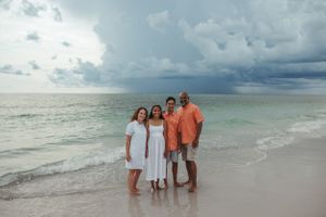 A group poses on a beach with dramatic storm clouds gathering over turquoise waters.