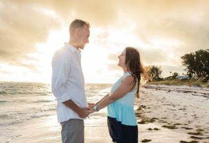 Couple holds hands while sharing romantic moment on beach at sunset.