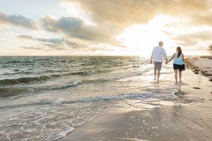 Couple walking along shoreline at sunset with waves crashing on beach.