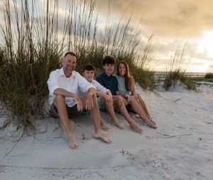 Group sitting together in beach dunes at sunset with sea oats in background.