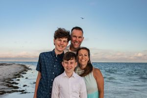 Group poses for beach portrait with ocean and seabird in background at sunset.