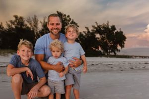 A beach family portrait during sunset with coastal vegetation in the background.