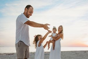 Happy group in white clothing plays together on beach at sunset.
