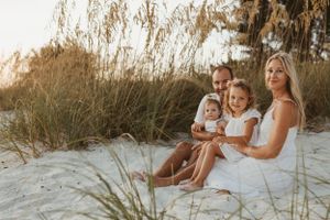 A family portrait on a beach with sea oats during golden hour.