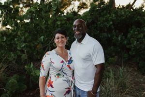 A couple stands outdoors in front of lush green foliage during a summer photoshoot.