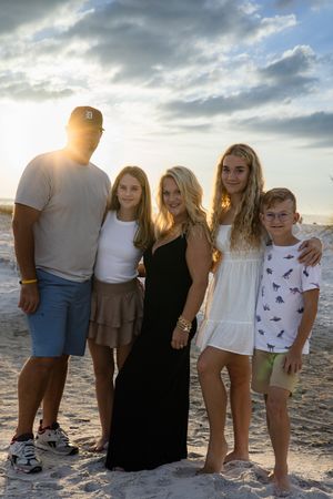 Family beach portrait with dramatic sunset lighting and coastal dunes in the background.