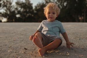 A toddler sits on sandy ground during golden hour.