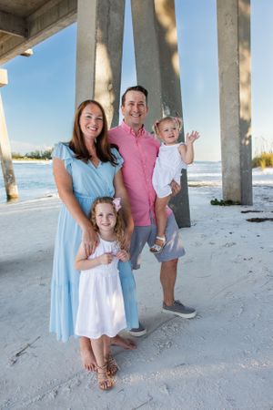 Family portrait under pier columns at the beach on a sunny day.
