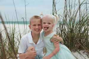 Two children smiling among beach grass with ocean in background.