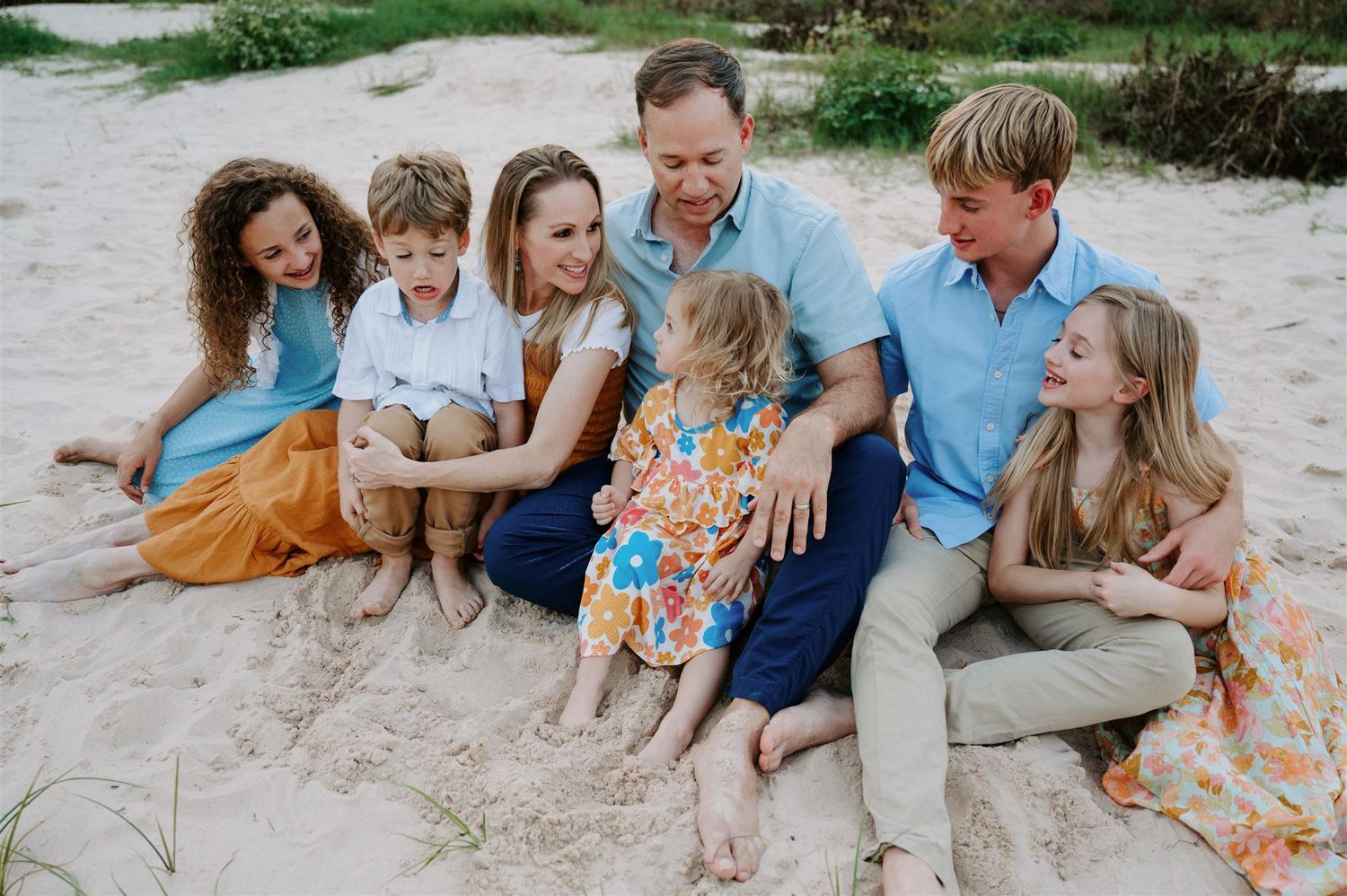 A joyful family cuddles close together during an outdoor photo session on sandy ground.