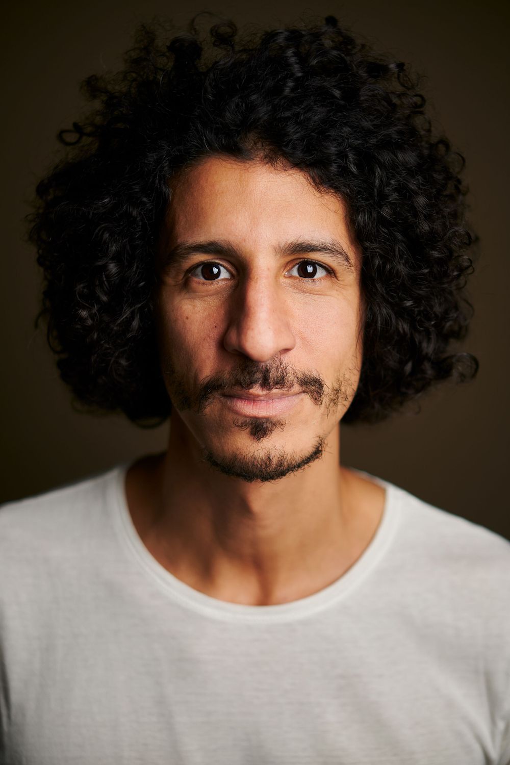 Studio portrait of a person with curly hair wearing a white t-shirt.