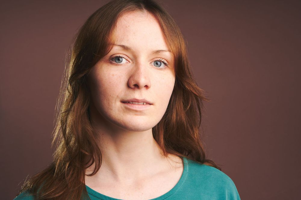 Professional headshot with soft lighting and teal top against warm background.