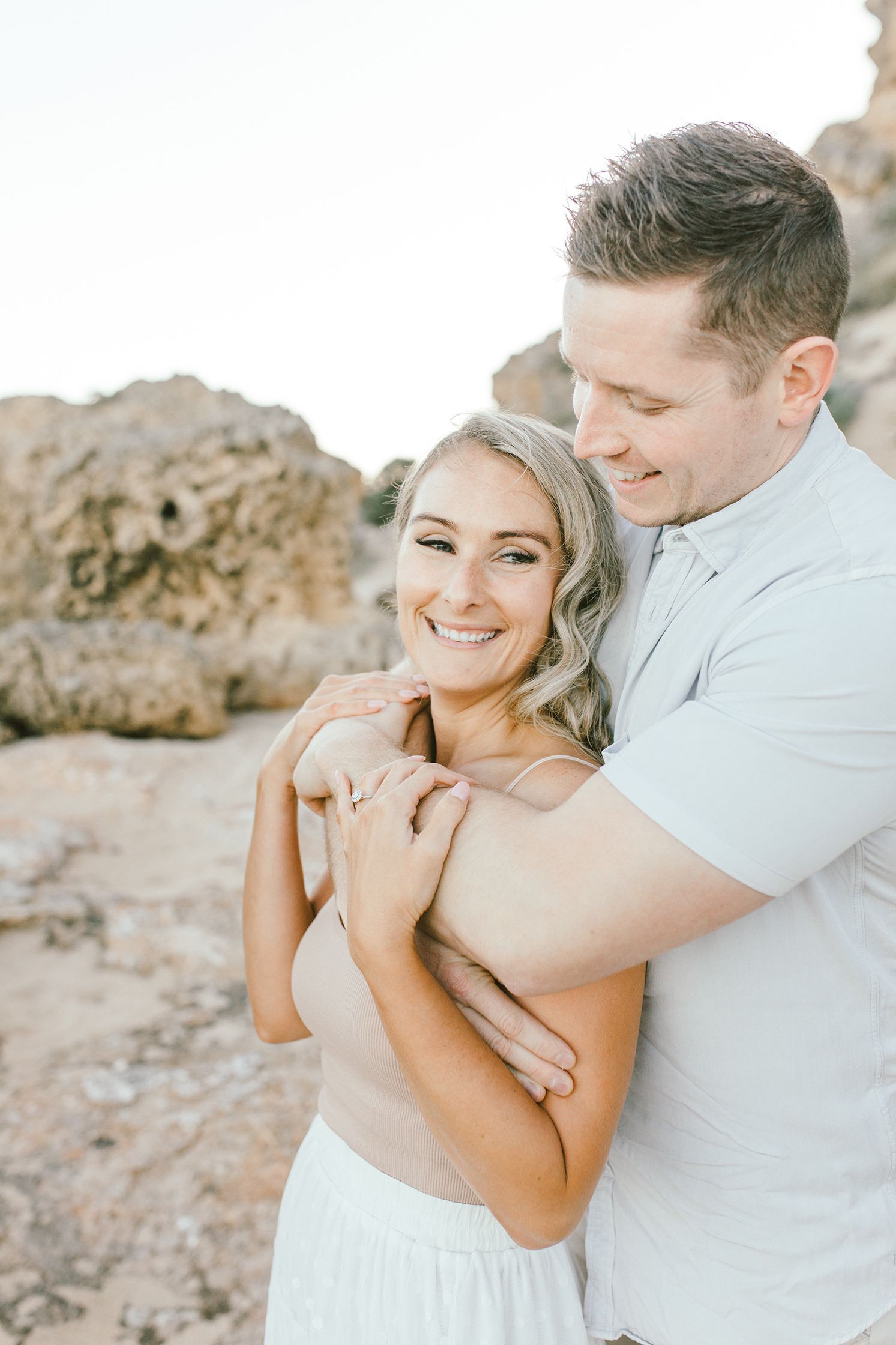 A loving couple shares a joyful moment against coastal rocks during golden hour.