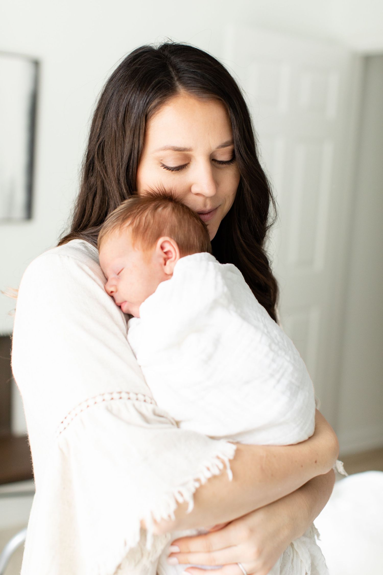 Tender embrace between parent and sleeping infant dressed in white.