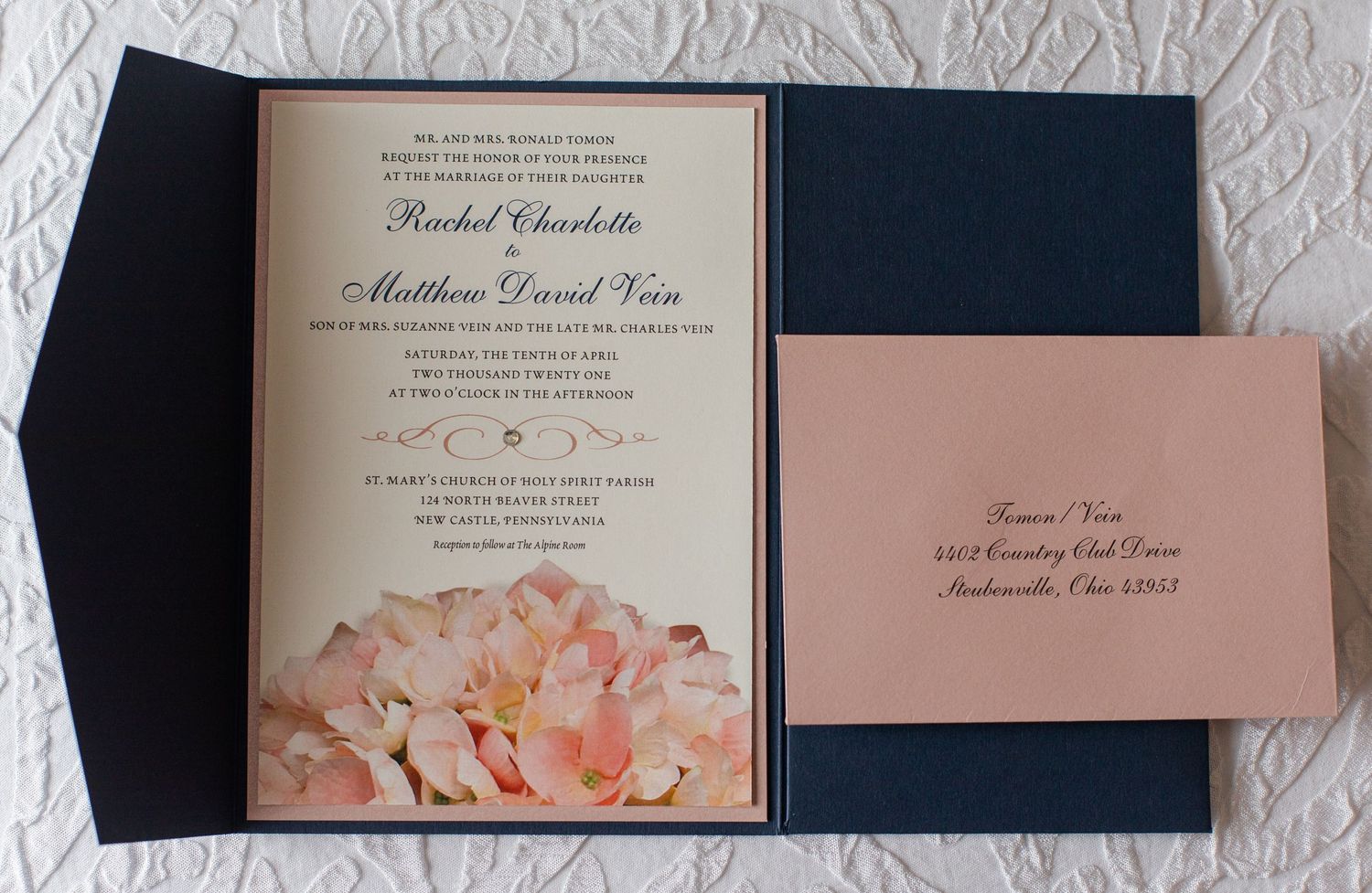 Elegant wedding invitations with navy blue and blush pink color scheme laid out on textured white surface.