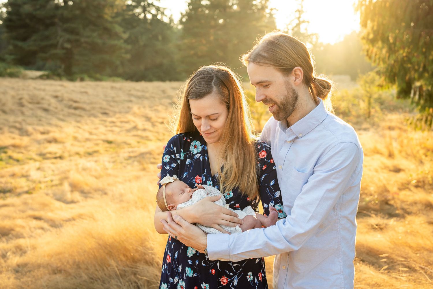 Parents hold newborn daughter in a grassy field at sunset