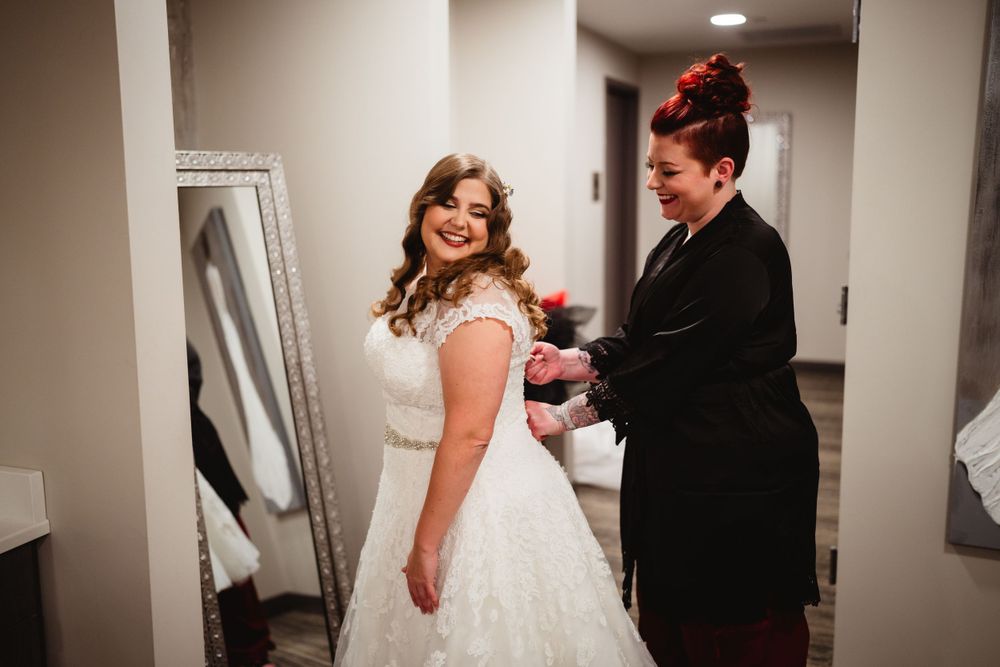 A bride getting final adjustments made to her wedding dress in a dressing room.
