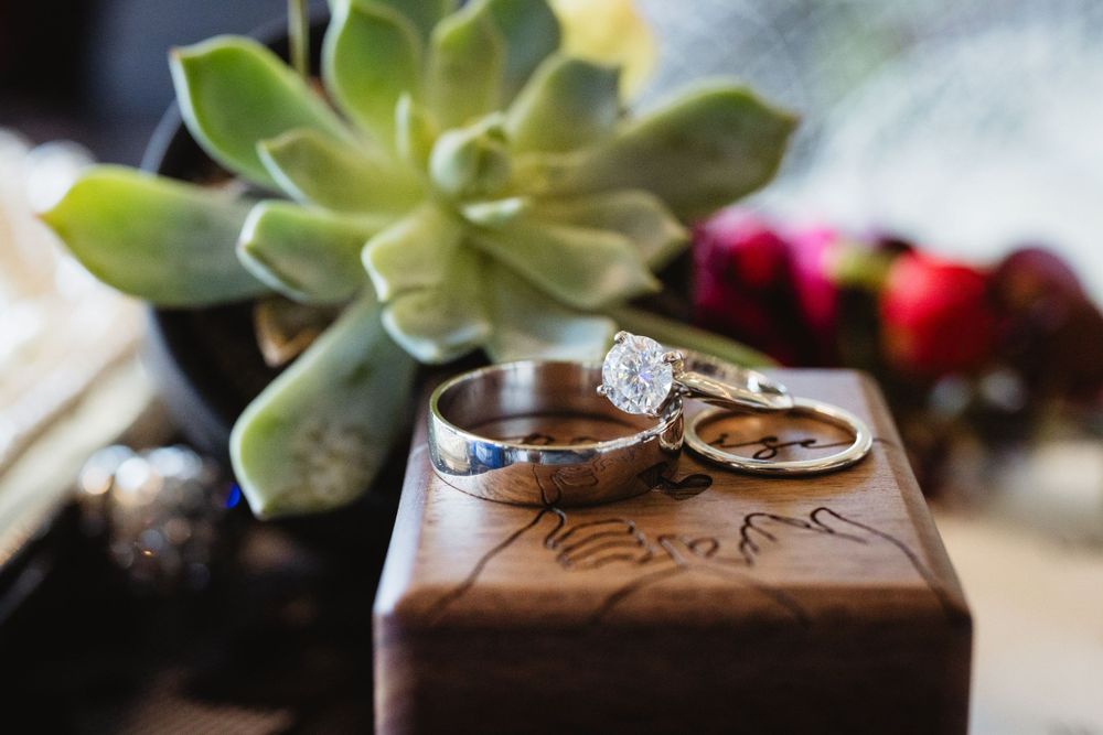 Wedding rings and engagement ring displayed on a wooden box next to a green succulent plant.