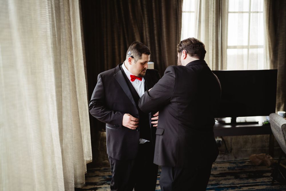 Two people in dark suits making final adjustments before formal event.