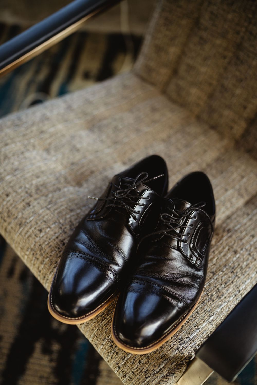 Polished black leather dress shoes placed on a beige textured surface.