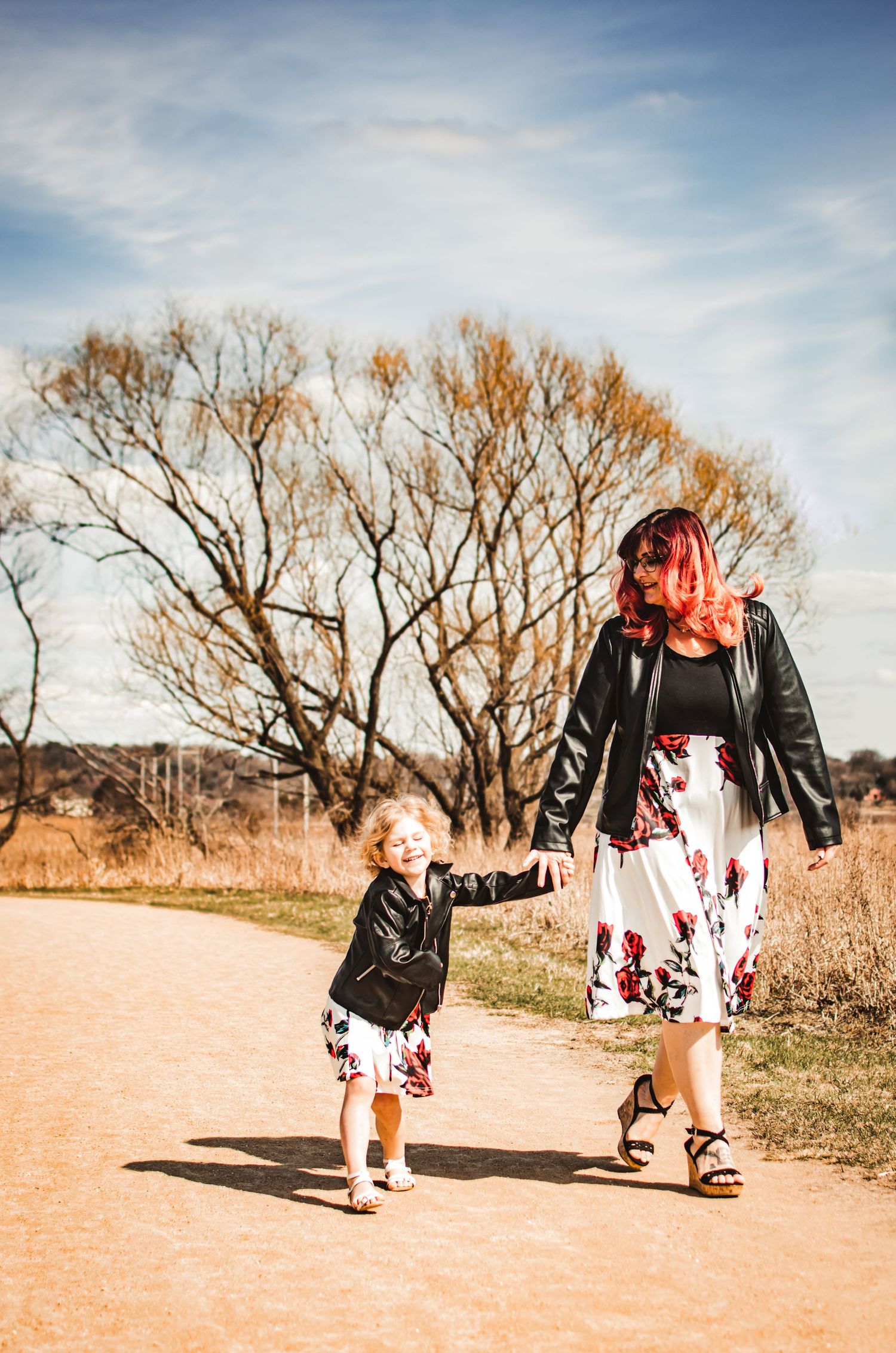 A matching pair walk hand in hand down a nature trail in coordinated floral outfits.