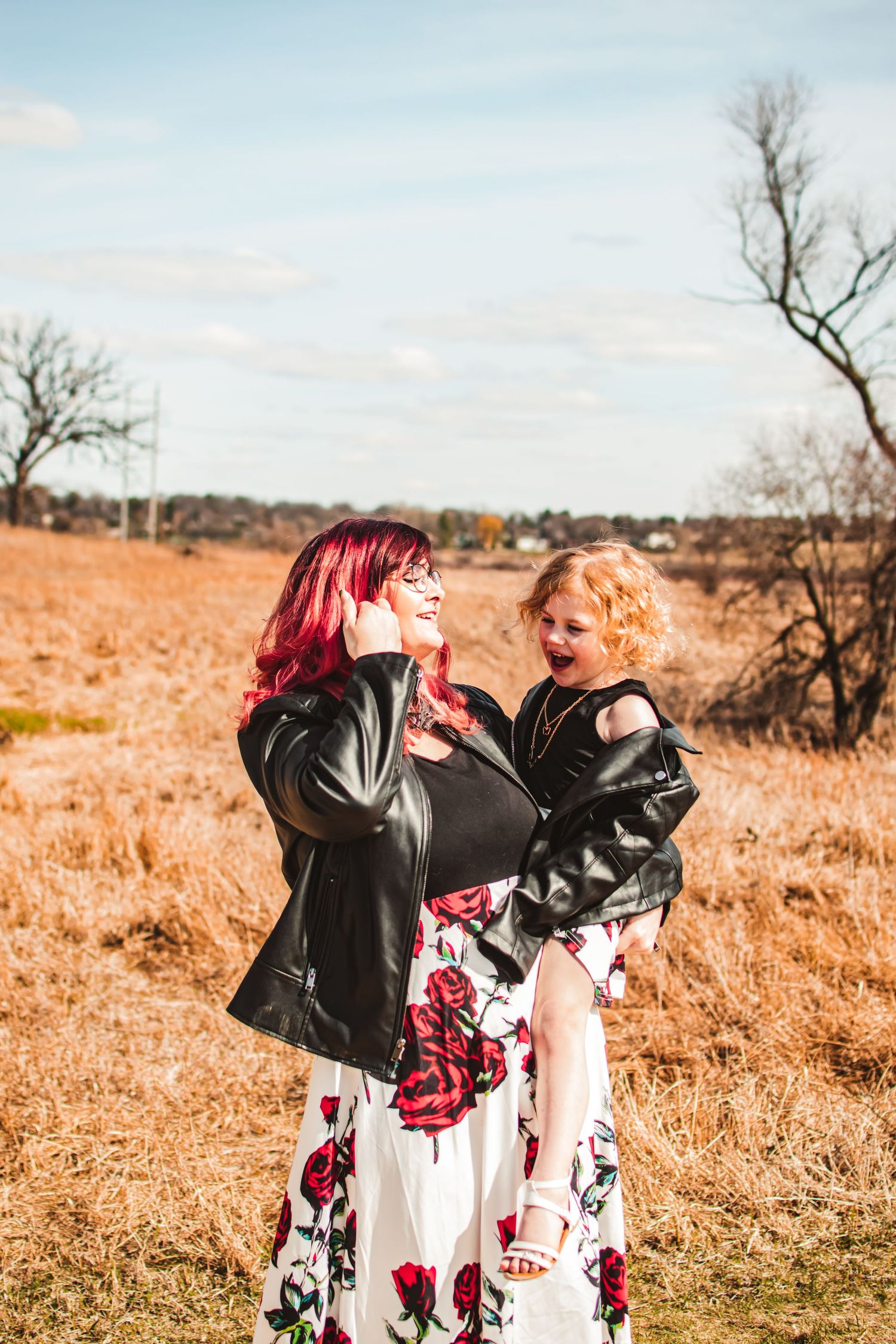 A tender outdoor moment between parent and child wearing matching floral dresses and leather jackets.
