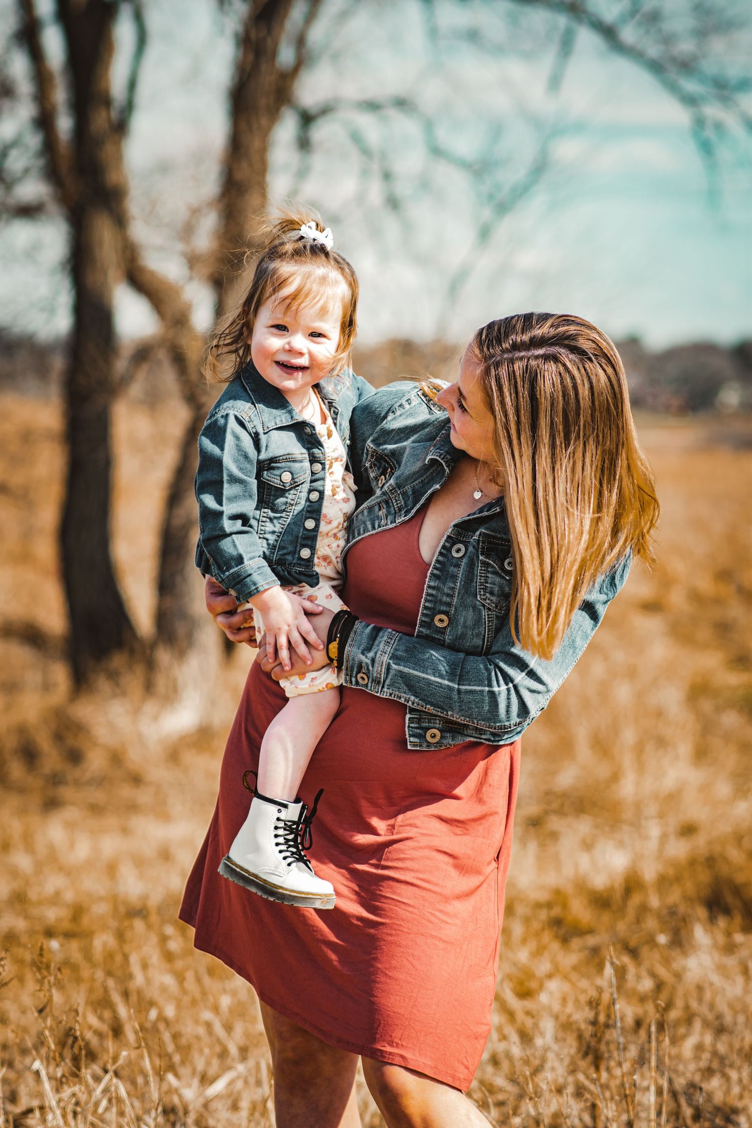 A pair in denim outfits share a tender moment in a sunlit field.
