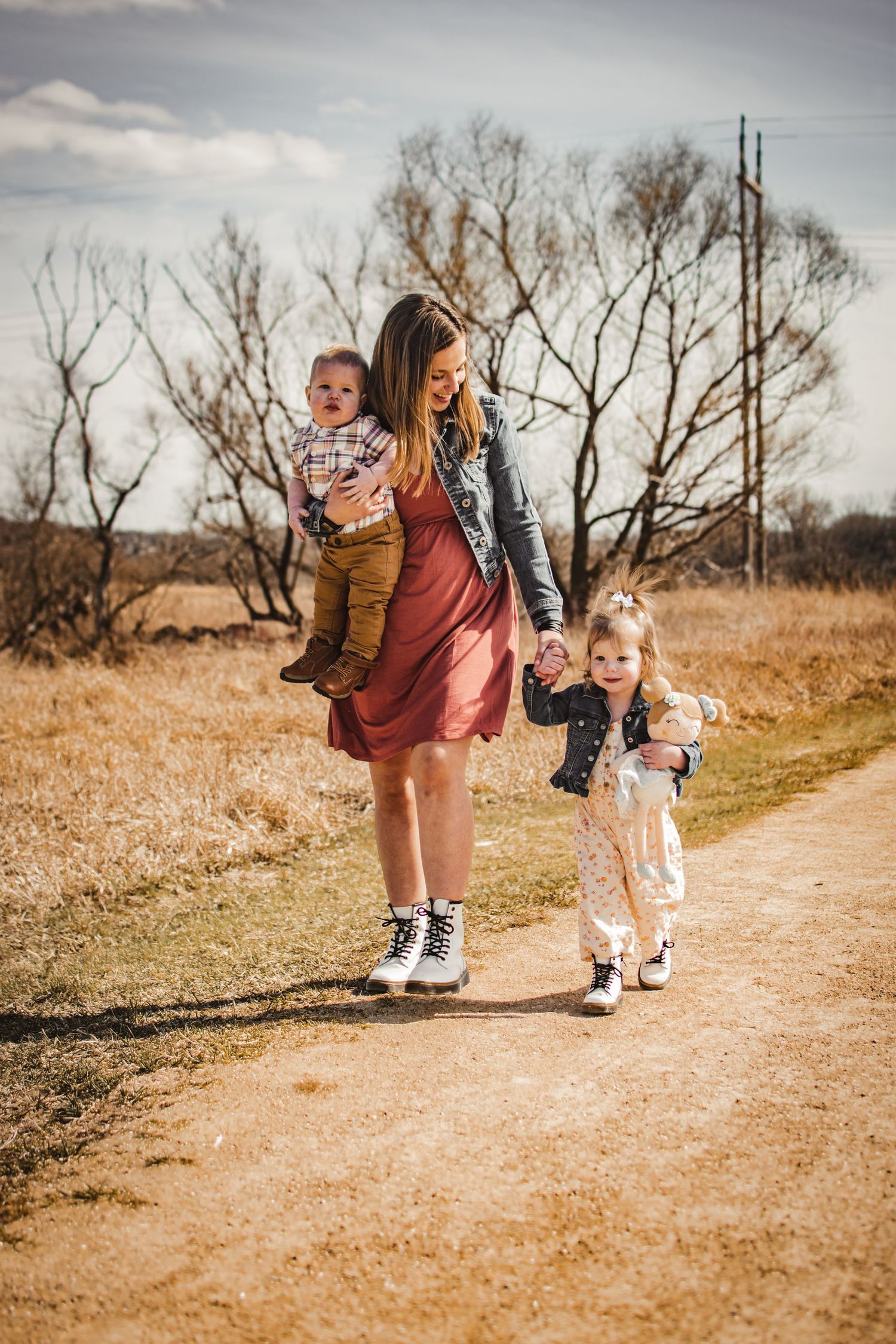Three people in casual attire walk together on a dirt path surrounded by bare trees.