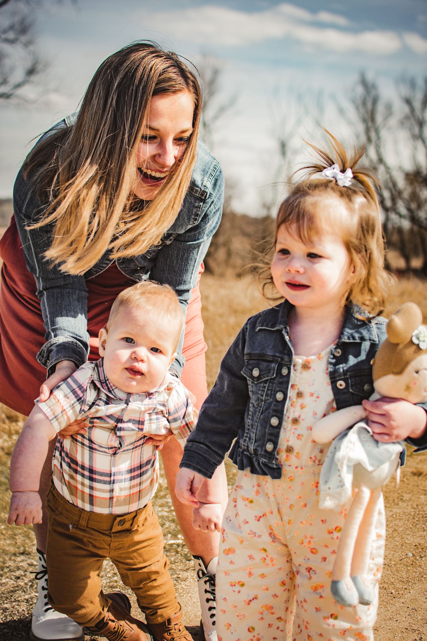 A joyful outdoor family moment on a dirt path with casual denim and plaid outfits on a sunny day.