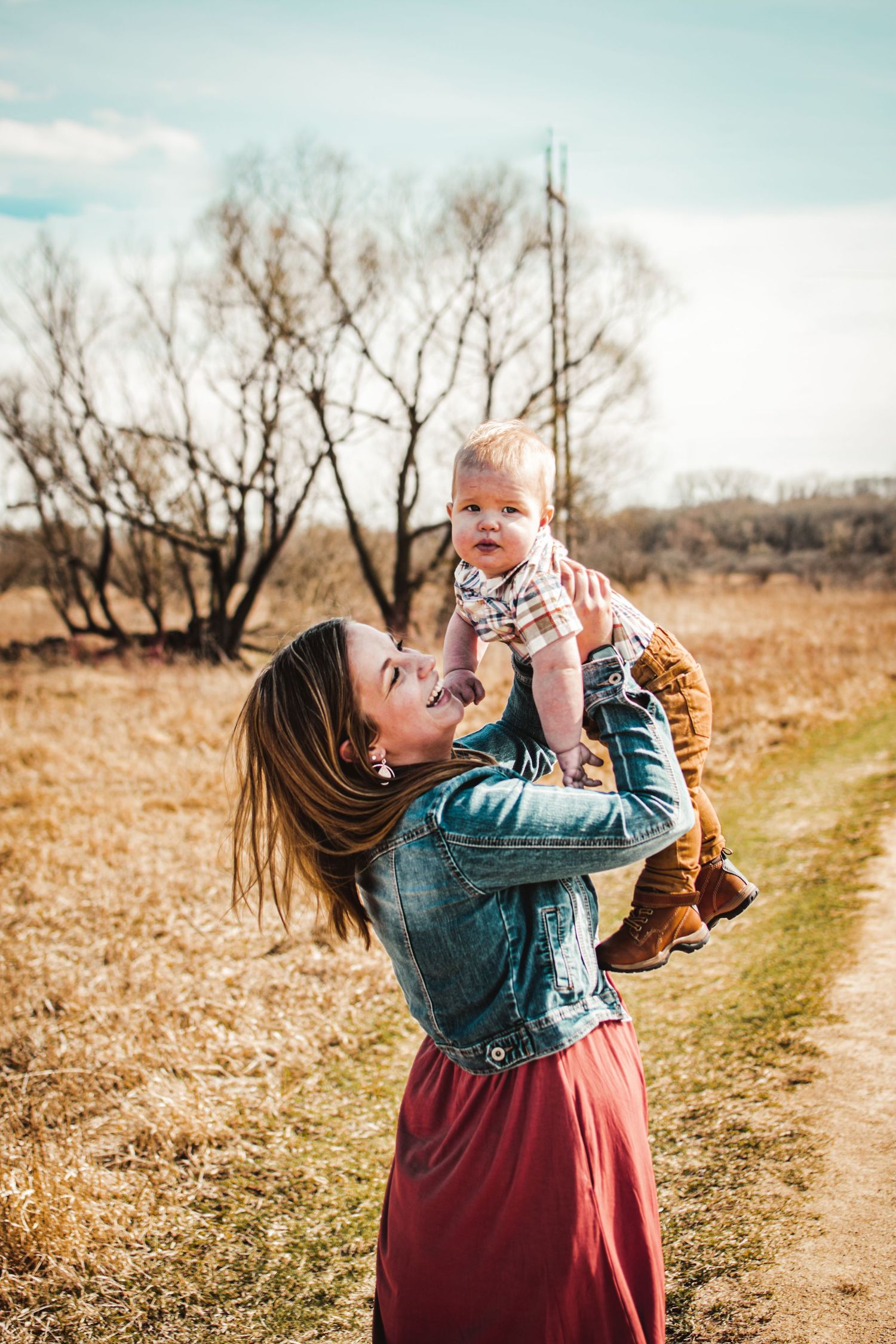 A heartwarming outdoor moment on a dirt path surrounded by bare trees on a bright day.