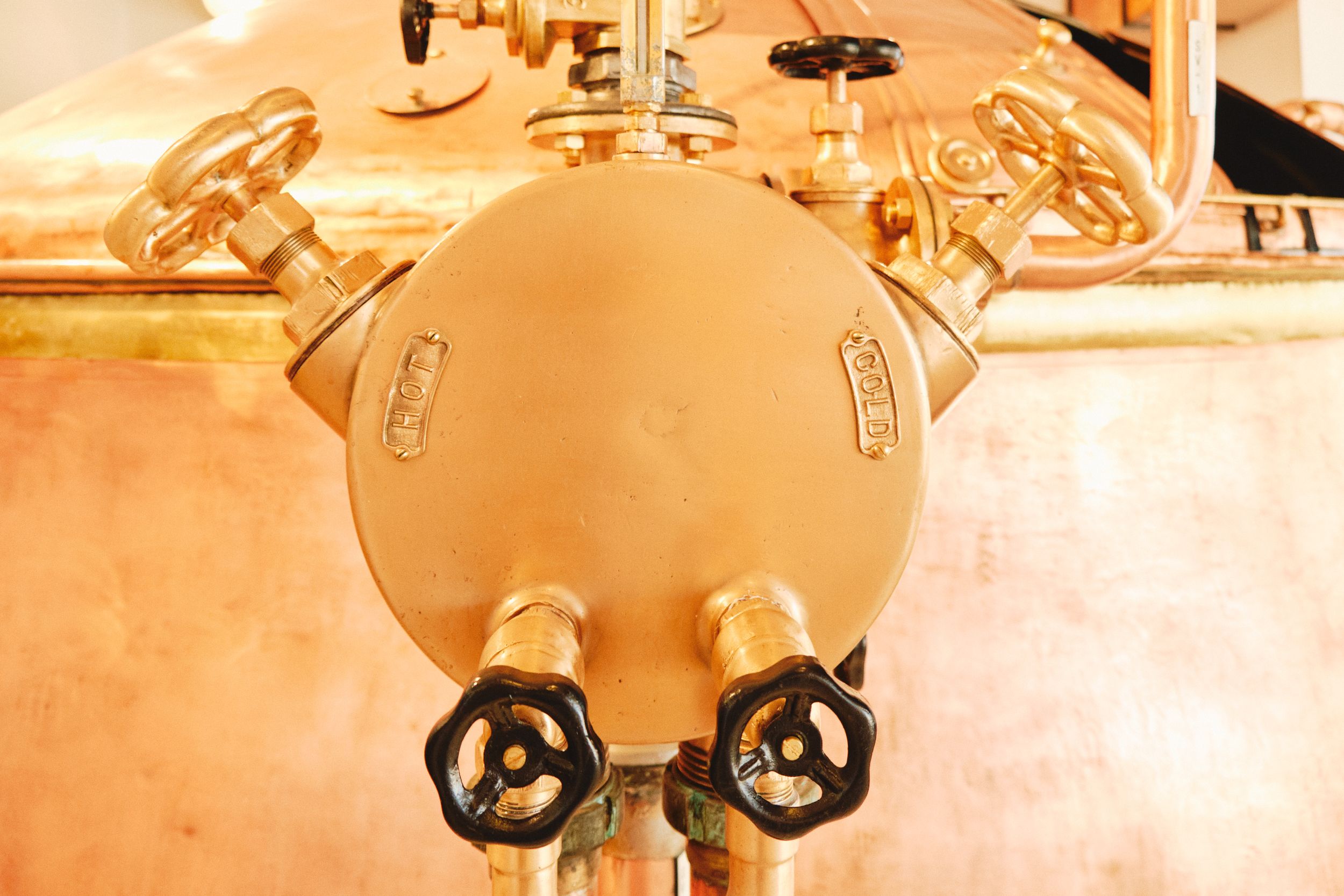 Close-up of industrial brewery tank valves and gauges in copper finish.