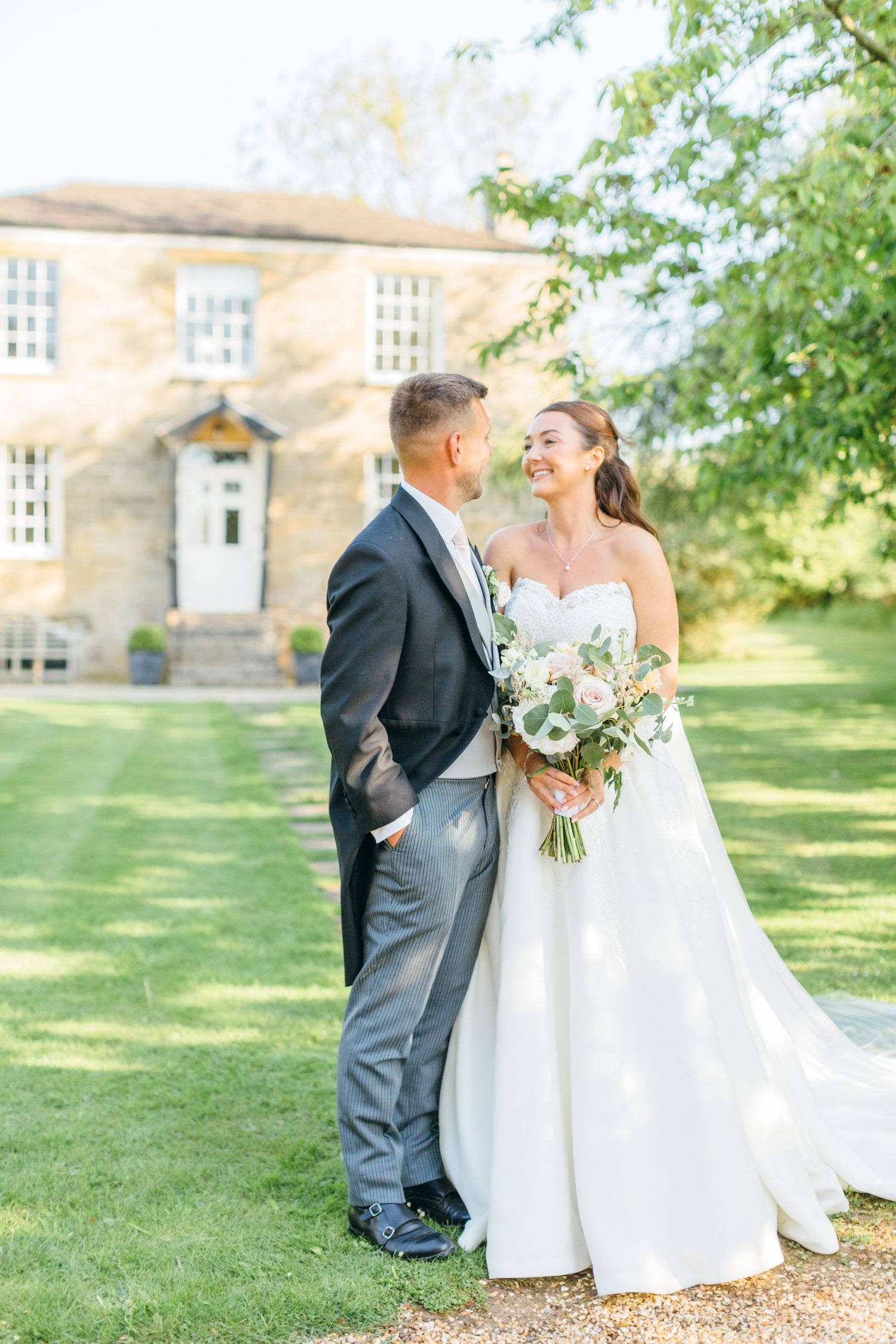 A couple shares a joyful moment on their wedding day in front of a stone country house.