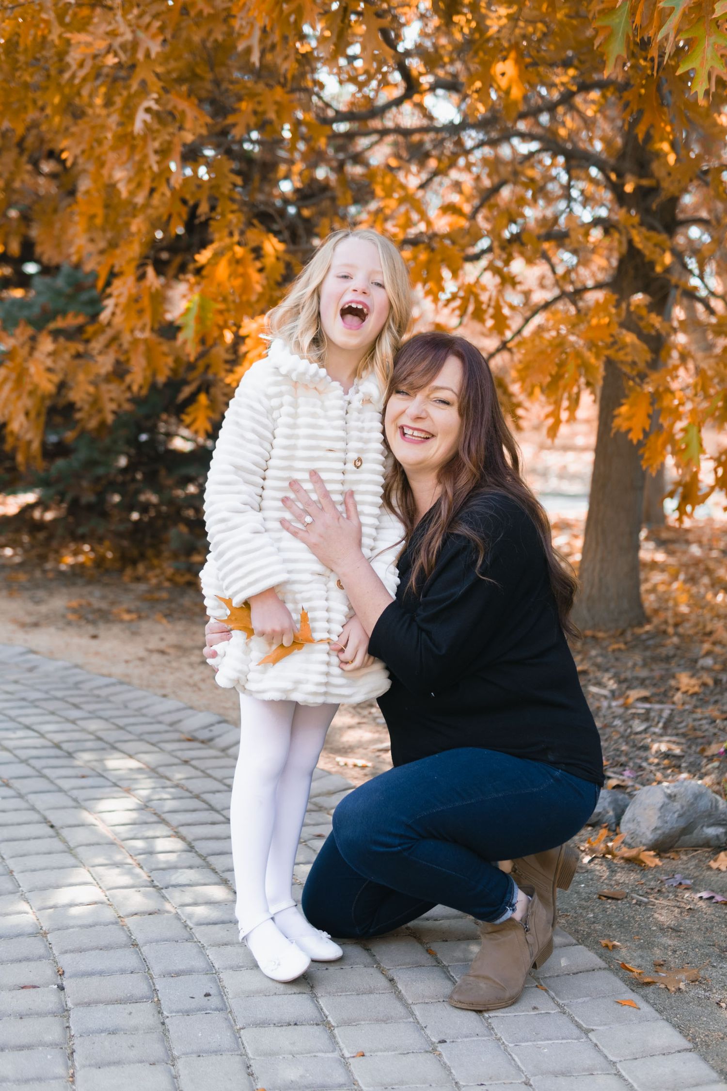 A joyful autumn scene with two people laughing together under golden orange fall foliage on a stone path.