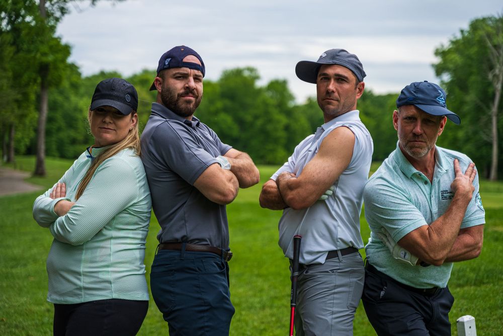 Four players strike confident poses on golf course path during cloudy day.