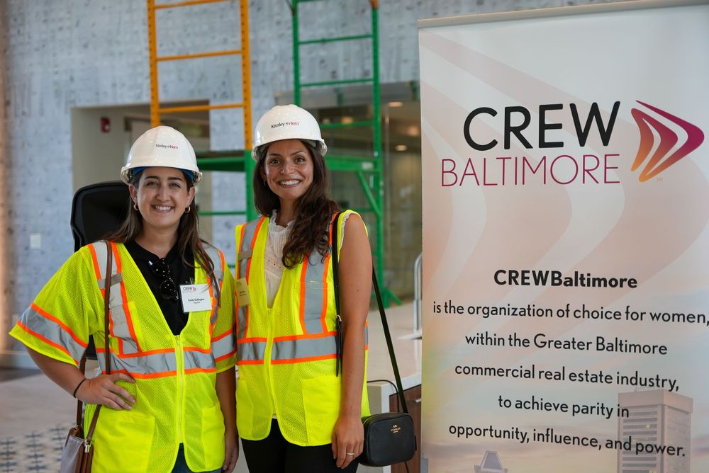 Construction workers in safety vests pose in front of CREW Baltimore banner at networking event.
