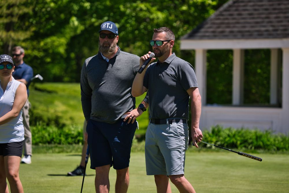Two golfers talking and laughing together on a sunny golf course with a gazebo in the background.