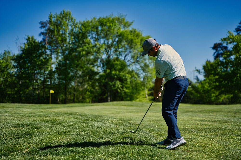 Golfer in white shirt and blue pants taking a swing on a lush green course.